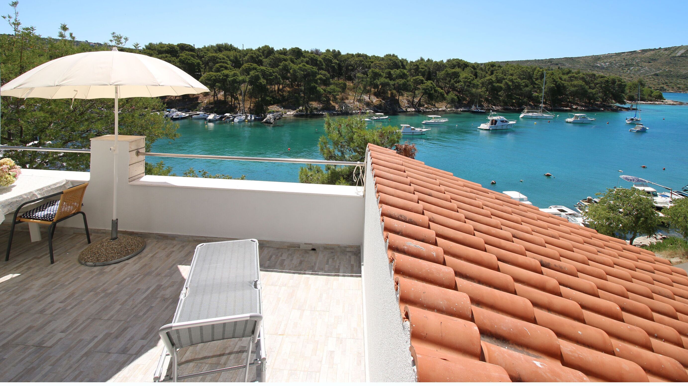A terrace with a table, chair, and umbrella overlooking a marina with boats.