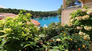 A balcony with a view of a marina, potted plants, and a clear blue sky. - Apartments Elvis (Primosten)