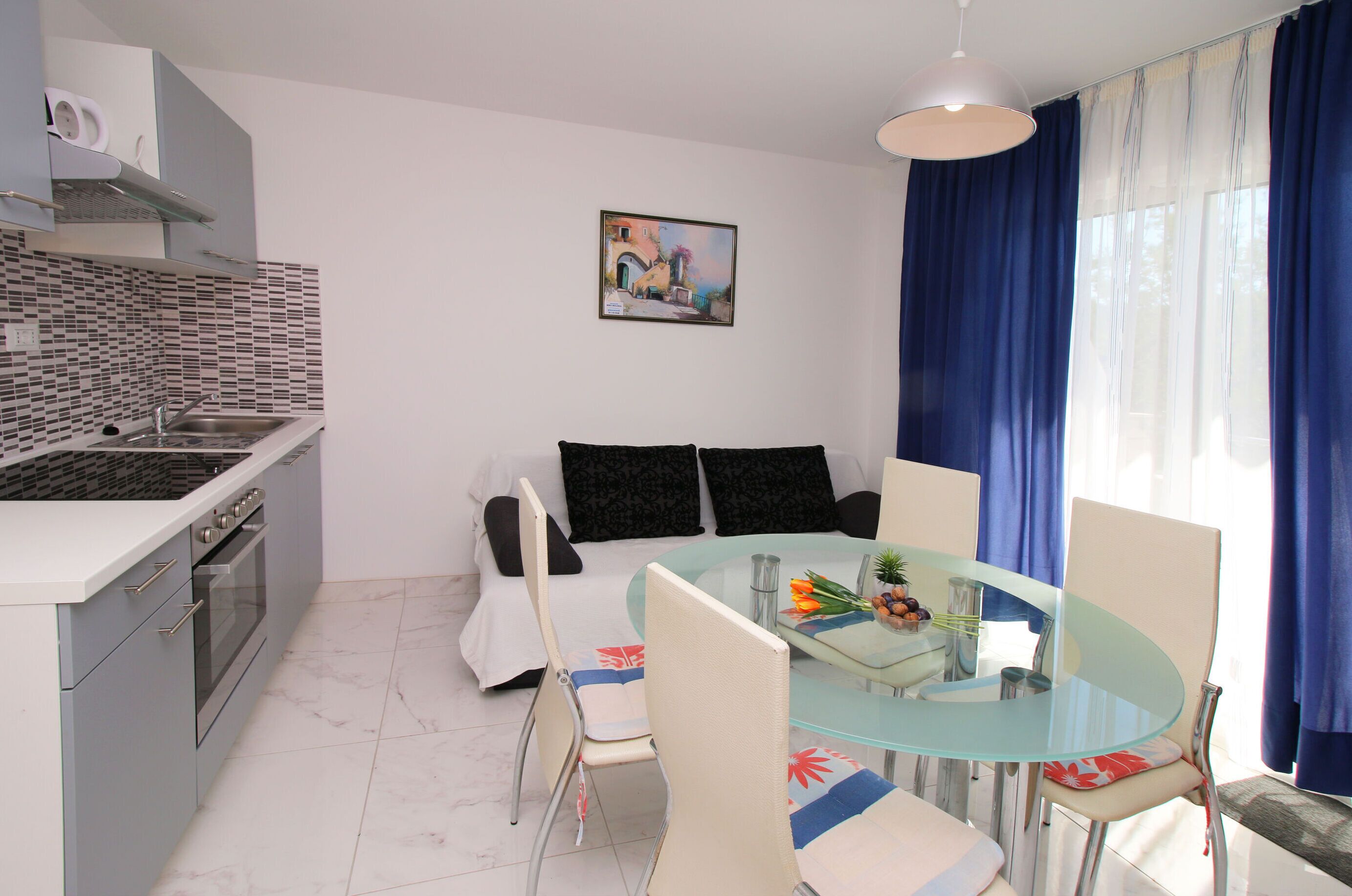 A compact kitchen with a modern stove, oven, and sink. A dining area with a glass table and chairs is adjacent to the kitchen.