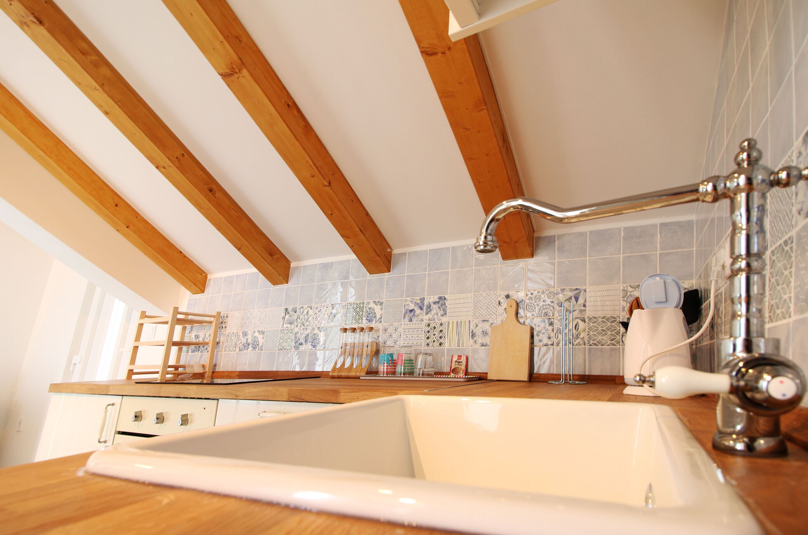 Una cucina con travi in legno, un lavello bianco e piastrelle a parete.