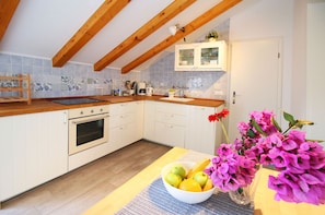 A kitchen with wooden beams, white cabinets, a tiled backsplash, and a fruit bowl on the counter. - Apartments Elvis (Primosten)