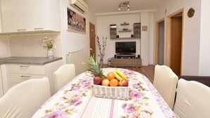 Un comedor con una mesa dispuesta para dos personas, una cesta de frutas y un televisor al fondo.