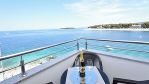 Un balcón con una mesa dispuesta para dos, con vista a un mar azul claro y una playa.