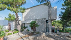 A modern building with a stone facade, a small garden with palm trees, and a clear sky. - Apartment Primosten Studio (Primosten)