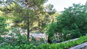 A stone retaining wall with lush greenery and trees in the background. - Apartment Primosten Studio (Primosten)