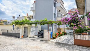 Un edificio residencial con entrada porticada, un automóvil estacionado y un jardín con plantas florecientes.