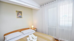 Una cama bien hecha con ropa de cama blanca y a rayas, una lámpara de noche y un cuadro en la pared.