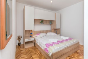 Un dormitorio con cama, mesitas de noche, tocador, espejo y estante con adornos.