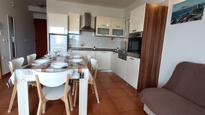 A modern kitchen with white cabinets, stainless steel appliances, and a dining area with a table set for six. - Apartments Antonia (Primosten)
