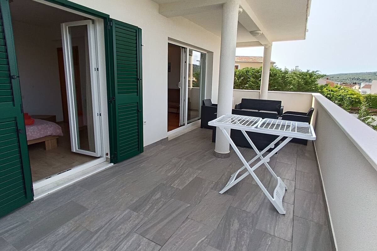 A balcony with a white folding table, green shutters, and a view of the surrounding area.