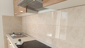 A modern kitchen with a black induction cooktop, a stainless steel sink, and beige marble tiles. - Apartments Antonia (Primosten)