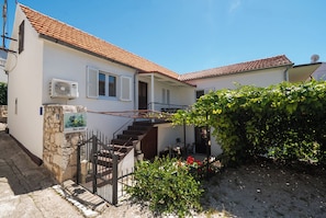A two-story house with a tiled roof, a staircase, a small garden, and a for sale sign. - Apartments Katica (Primosten)