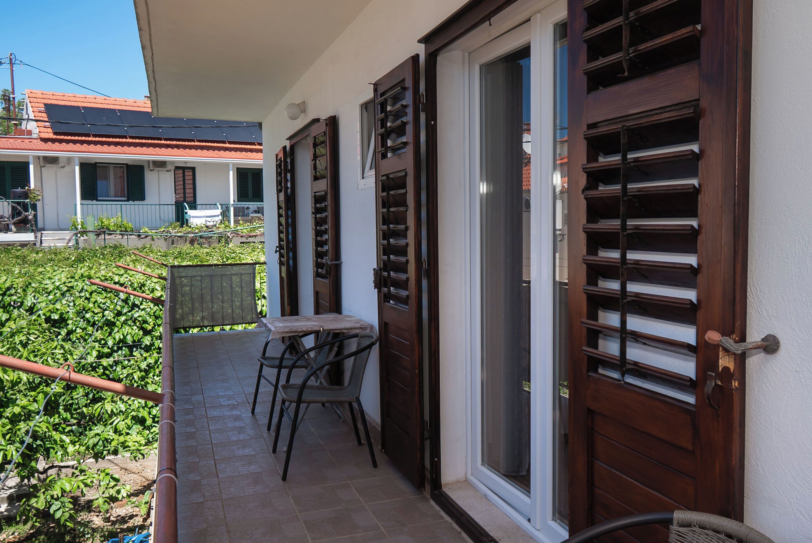 Un balcon avec une table et des chaises, une porte avec une fenêtre et un espace jardin.