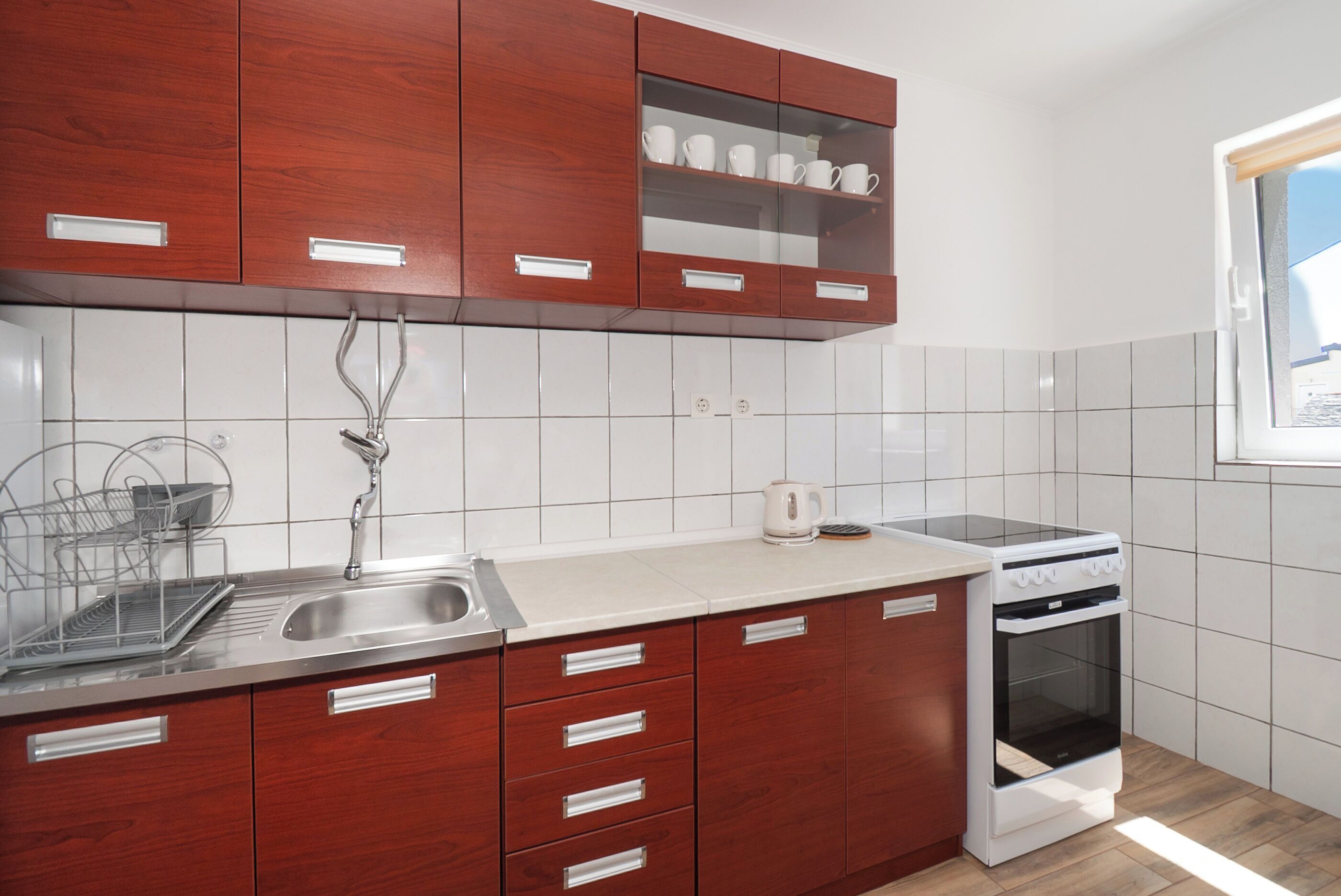 A kitchen with wooden cabinets, a stainless steel sink, a white countertop, and a built-in oven.