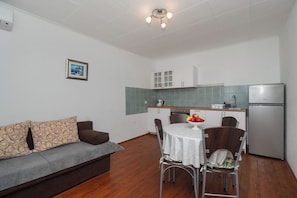 A compact living space with a sofa, dining table, chairs, a kitchen area with cabinets and a refrigerator. - Apartments Katica (Primosten)