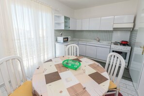 Une cuisine compacte avec des meubles blancs, un four à micro-ondes, une cuisinière et une table à manger avec des chaises.