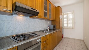 Una cocina con armarios de madera, estufa a gas, microondas y una ventana con persianas.