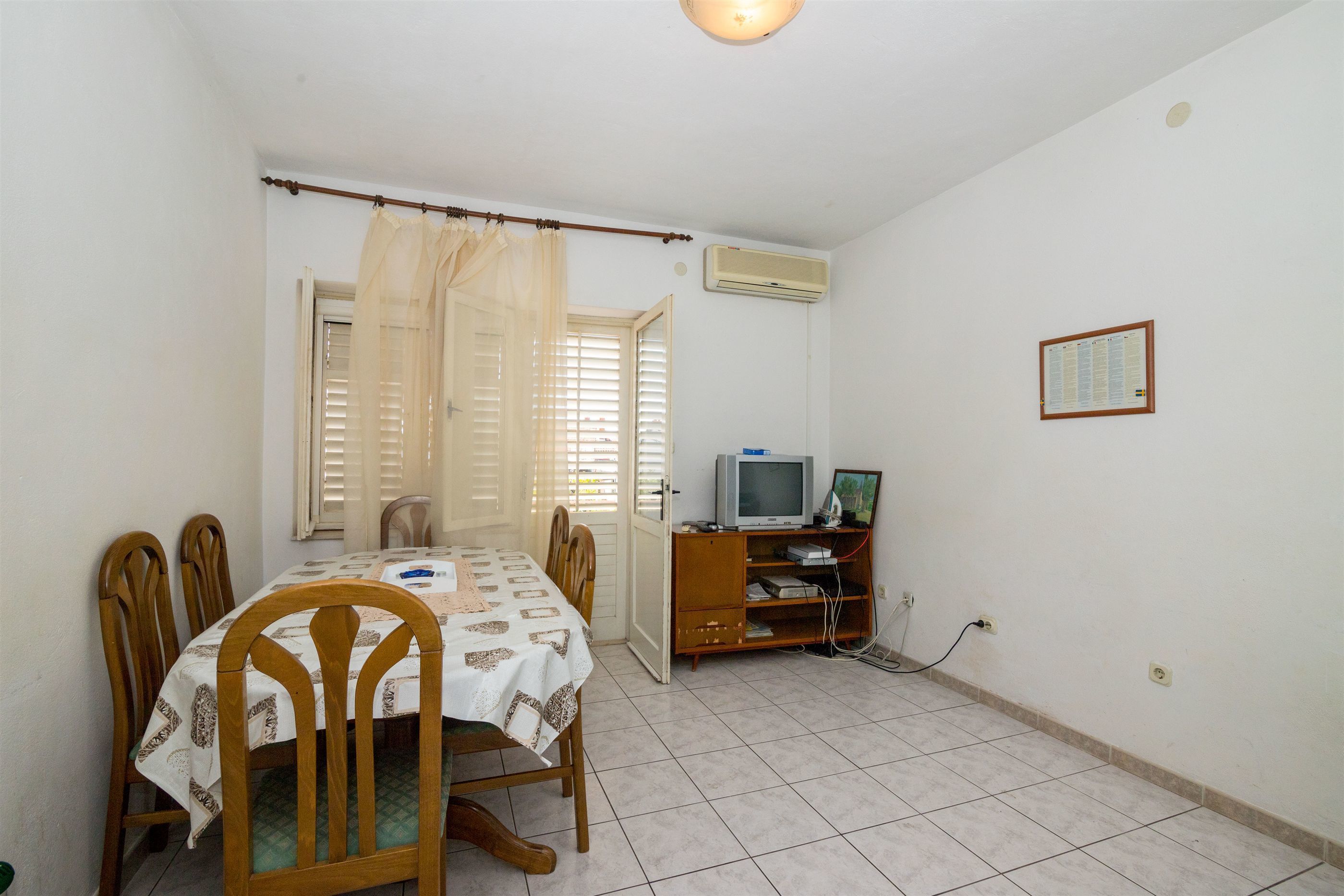 A dining area with a table set for four, a television on a stand, and an air conditioning unit on the wall.