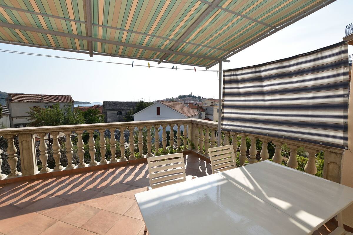 Ein Balkon mit Tisch und Stühlen, einem gestreiften Sonnenschirm und Blick auf Gebäude in der Ferne.