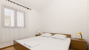 A neatly made bed with white linens, two bedside tables with lamps, and a window with sheer curtains. - Apartment Damir (Primosten)