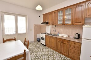 A kitchen with wooden cabinets, a stove, a sink, and a refrigerator. - Apartment Damir (Primosten)