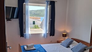 A bedroom with a bed, a TV, a window with curtains, and a view of buildings. - Apartments Vladimir (Primosten)