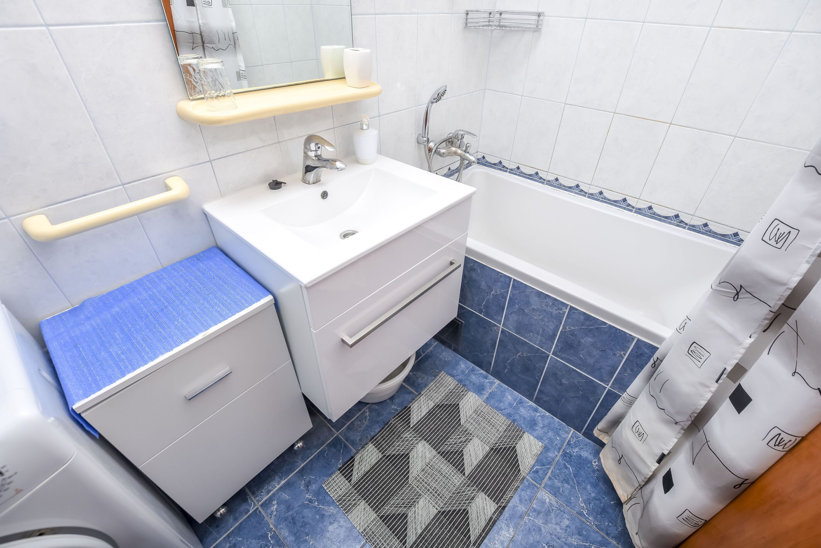 A bathroom with a white sink, mirror, and vanity, blue-tiled floor, and a shower curtain with a pattern.