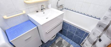 A bathroom with a white sink, mirror, and vanity, blue-tiled floor, and a shower curtain with a pattern.
