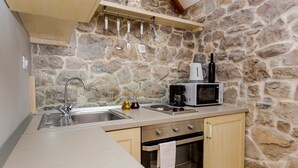 Een keuken met een stenen muur, een spoelbak van roestvrij staal, houten kastjes, een magnetron en een fornuis.
