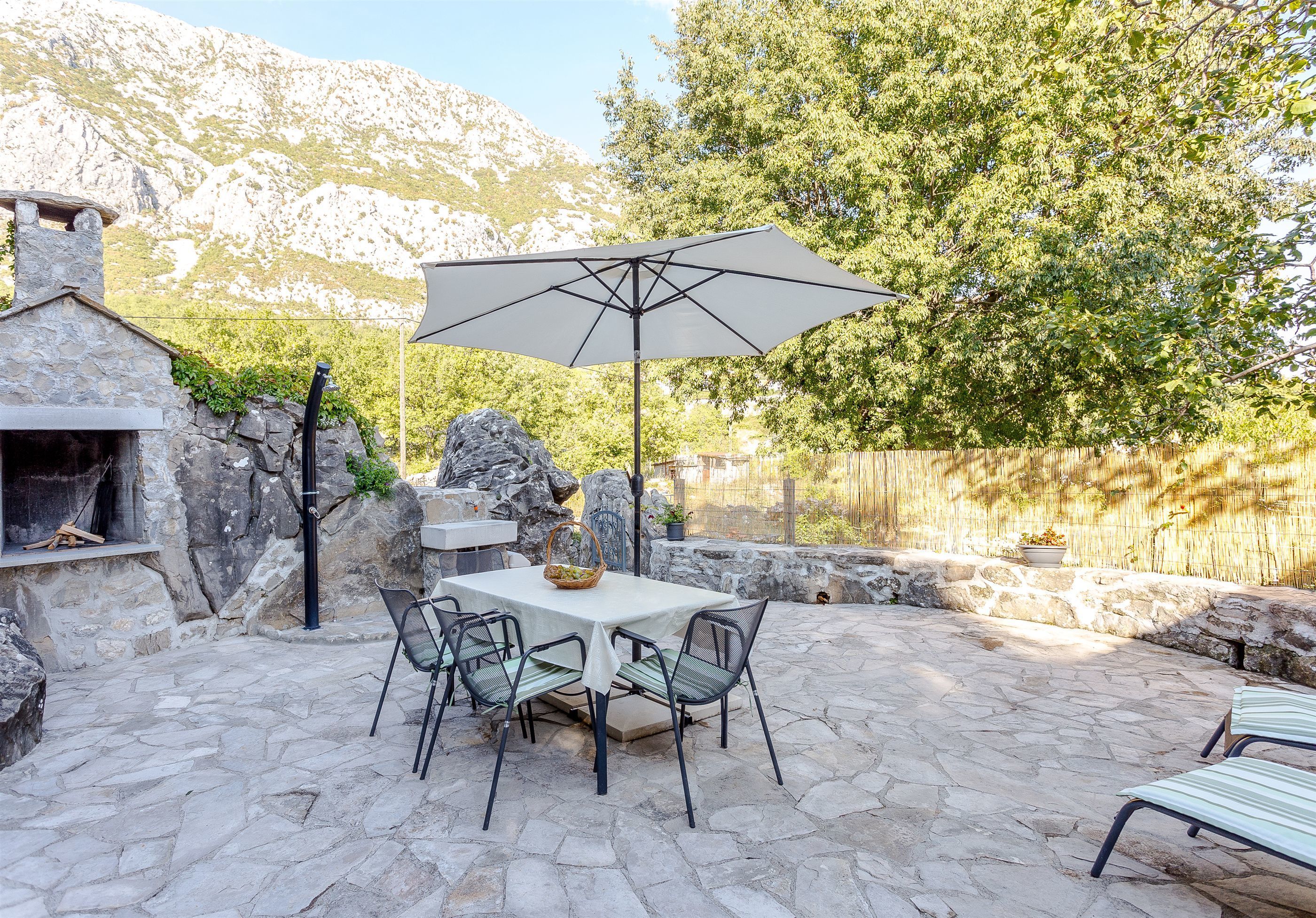 An outdoor patio with stone flooring, a table with chairs, a large umbrella, and a stone fireplace.