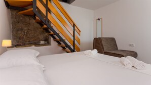 Een hotelkamer met een bed, een stoel, een lamp en een houten trap.