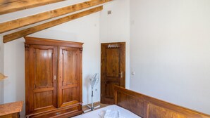 A bedroom with a wooden wardrobe, a bedside table, a bed with a white mattress, and a wooden ceiling beam structure. - House Sanda (Kastel Novi)