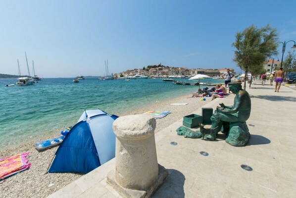 A coastal scene with a clear blue sea, boats, and a stone pillar.