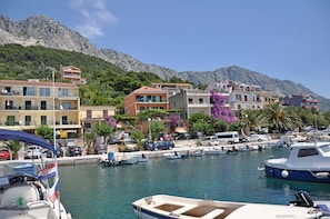 Un port de plaisance avec des bateaux, une chaîne de montagnes en arrière-plan et des bâtiments dotés de balcons.