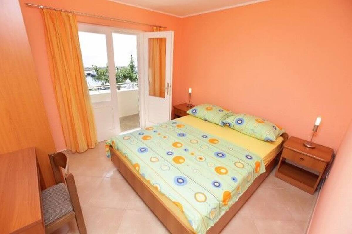 A bedroom with a bed, a nightstand, a chair, and a window with curtains.