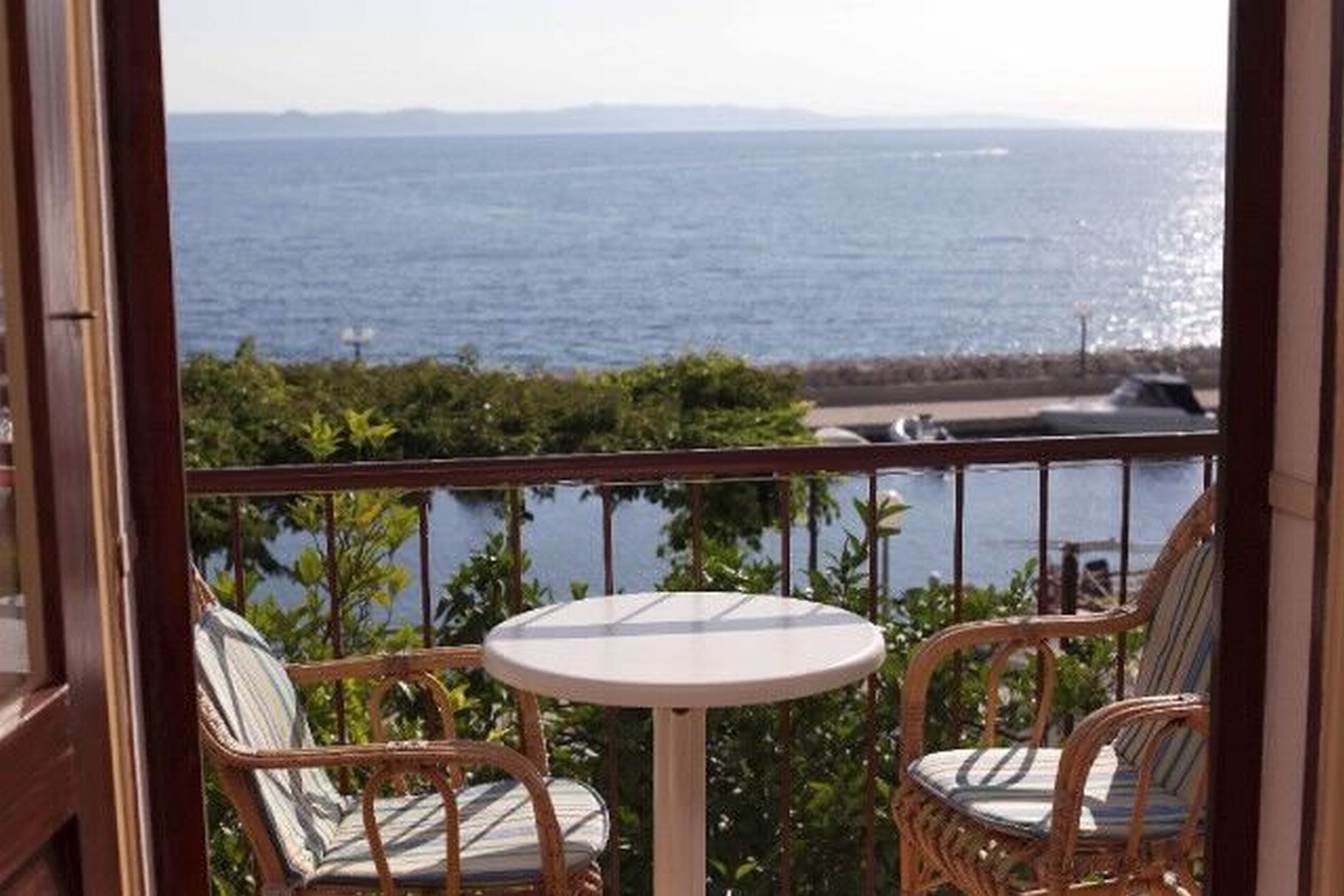 A balcony with wicker chairs and a small round table, overlooking a body of water and greenery.