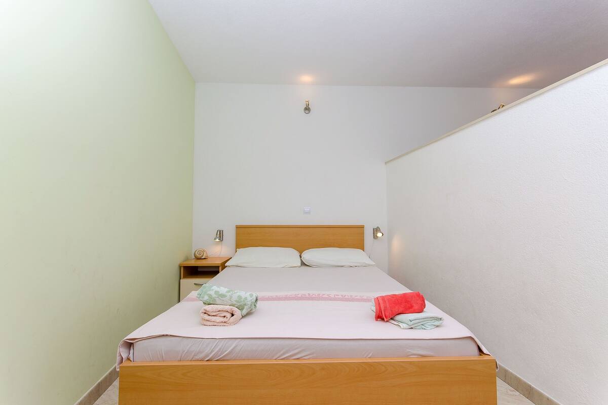 A single bed with a wooden frame, a nightstand, and a wall-mounted light fixture.