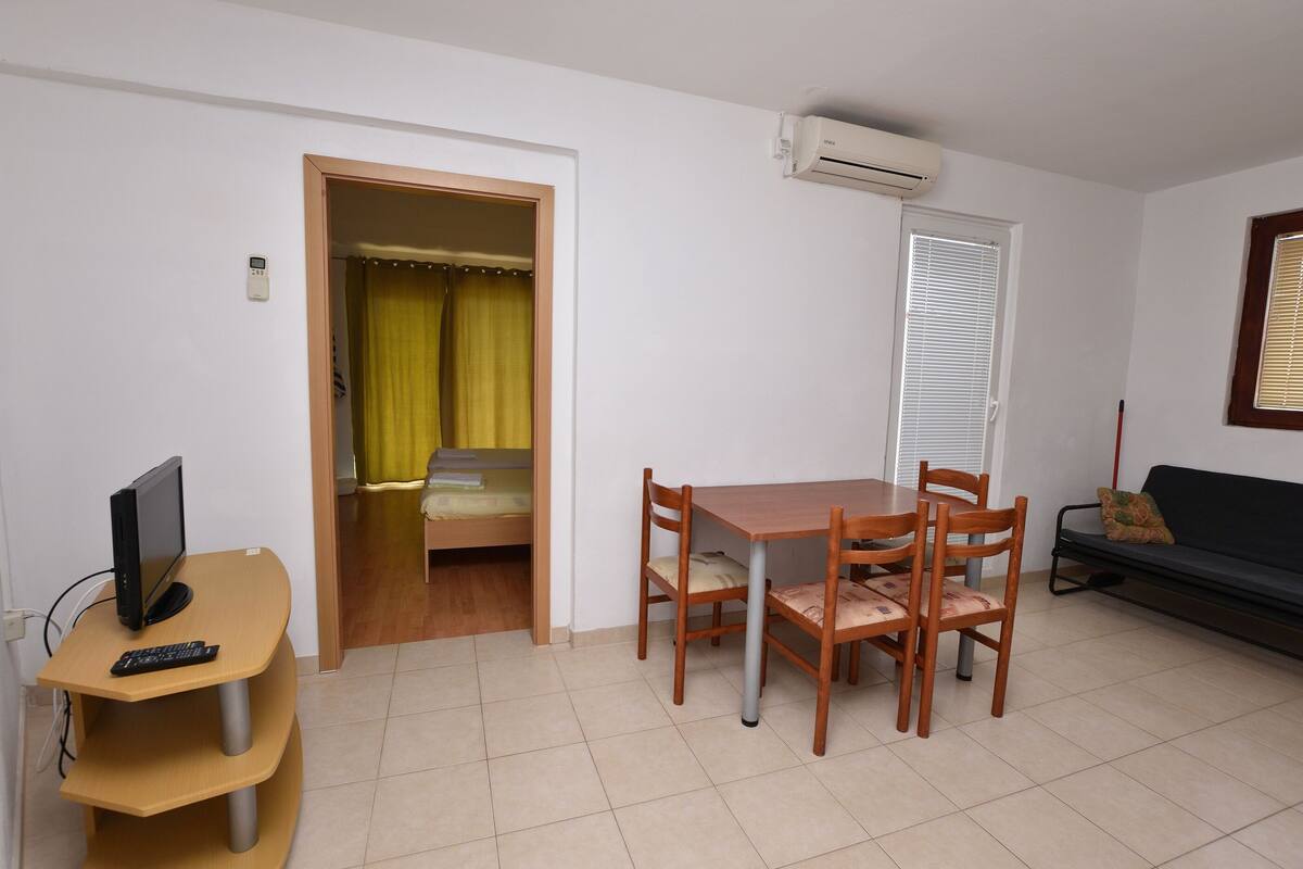 Un espace de vie compact comprenant une table à manger, des chaises, un canapé, un téléviseur et un lit à l’arrière-plan.