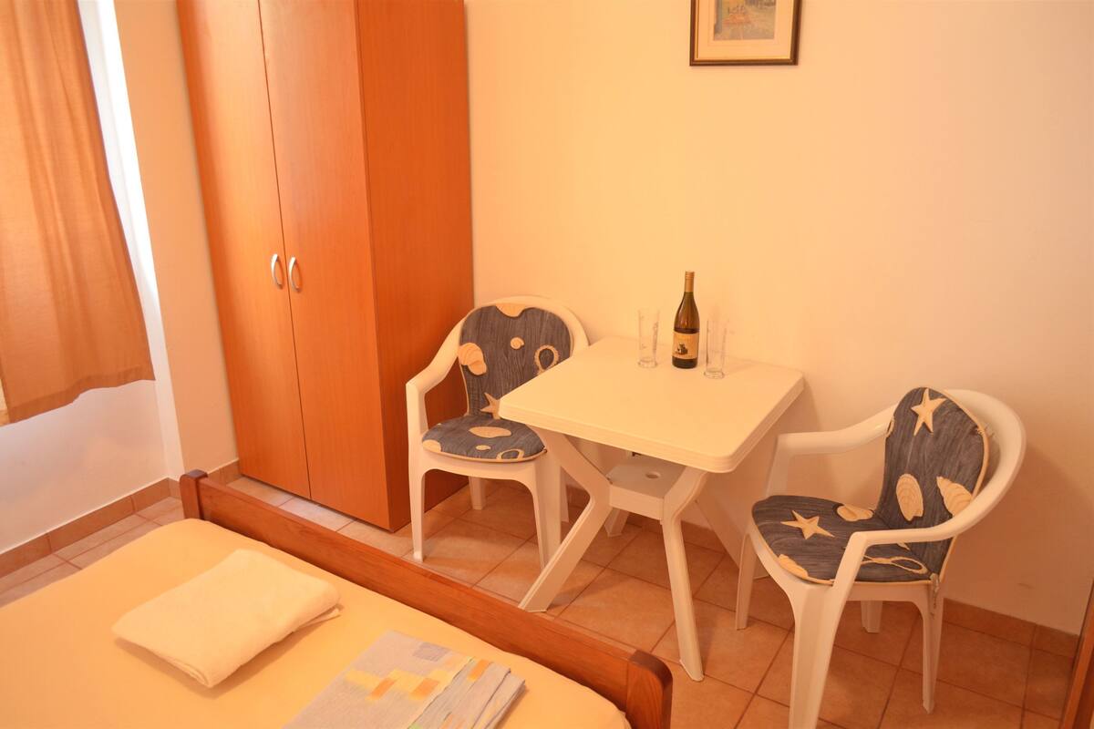 Une pièce avec un lit, une table entourée de chaises, une bouteille et un tableau encadré accroché au mur.