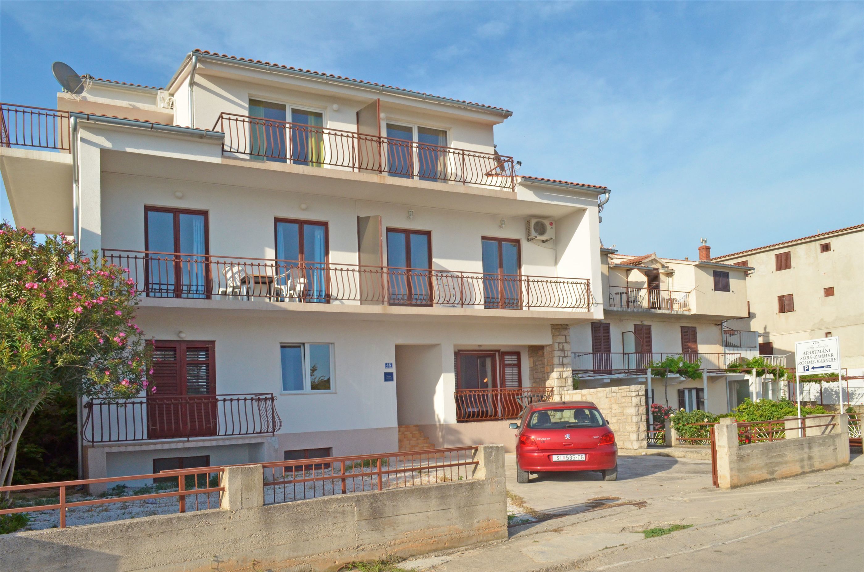 A two-story building with balconies, a red car parked in front, and a sign indicating a 2-star rating.