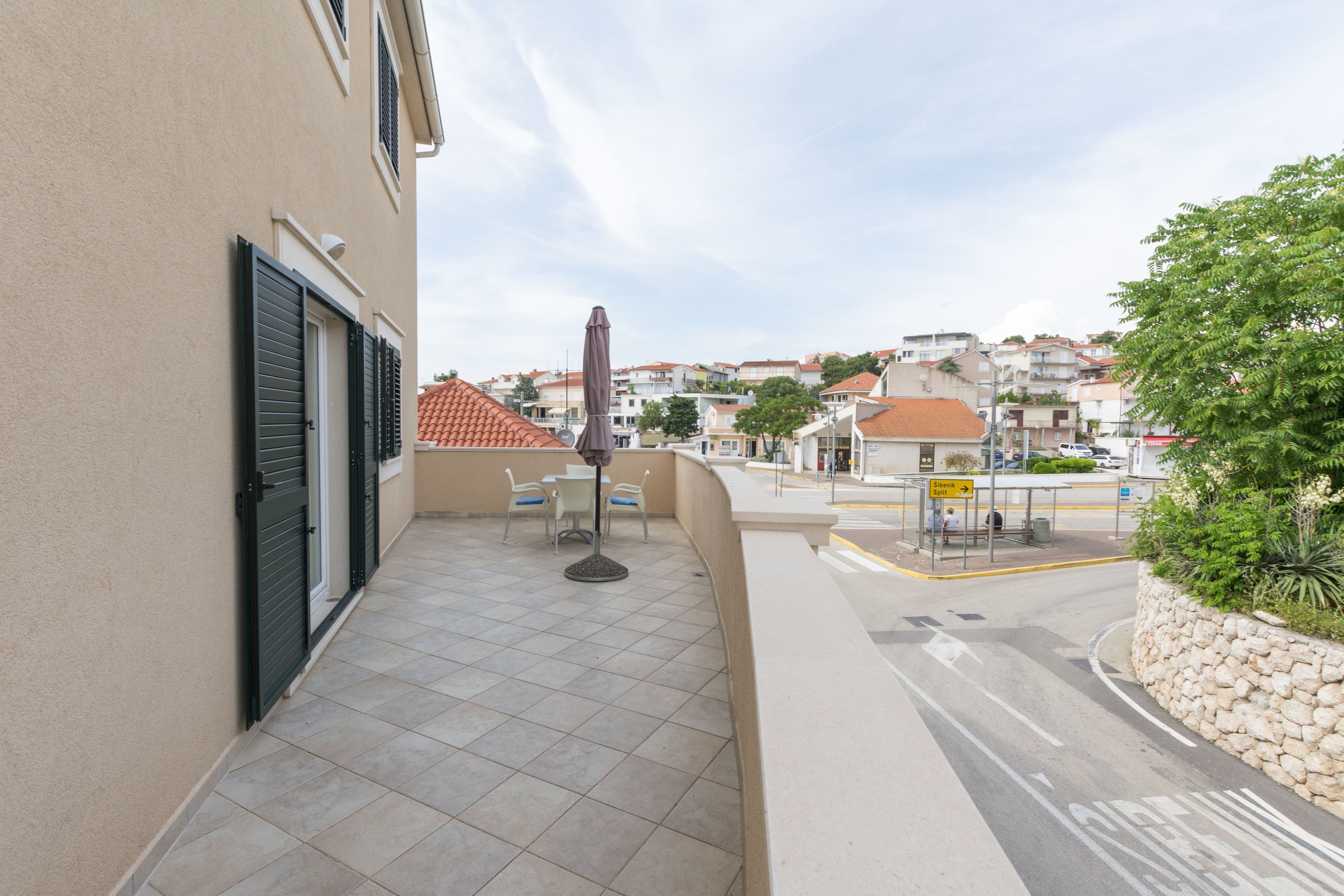 Ein Balkon mit Tisch und Stühlen, Blick auf die Straße und ein Schild, das eine Bushaltestelle anzeigt.