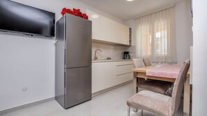 A compact kitchen with a refrigerator, a microwave, and a dining area with a table and chairs. - Apartments Frane (Primosten)