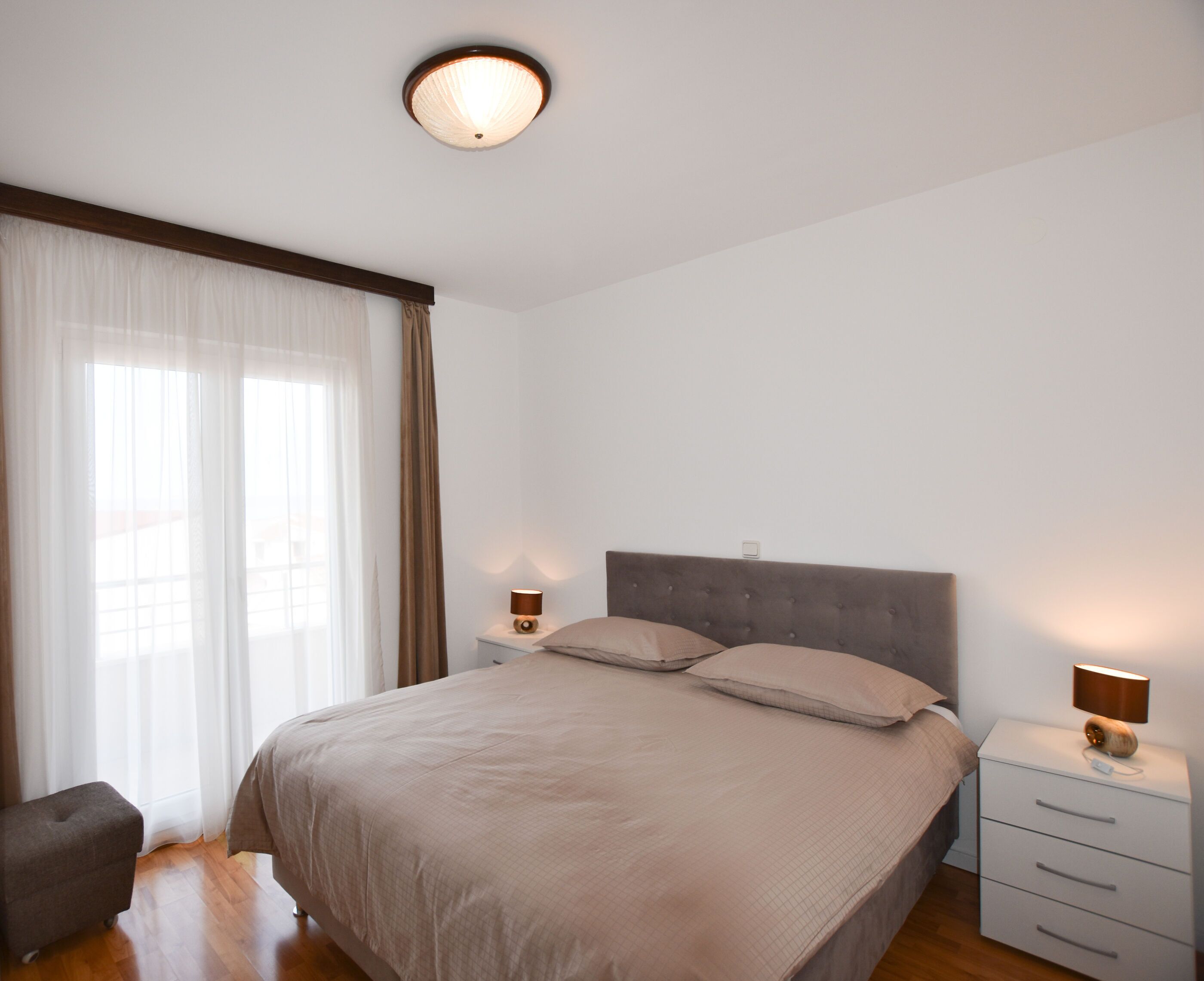 A bedroom with a large bed, two bedside lamps, a nightstand, and a window with curtains.