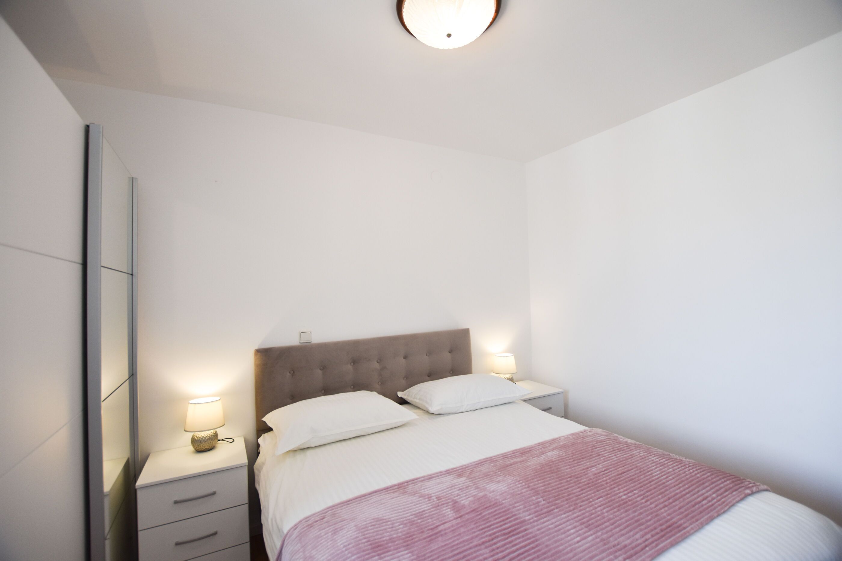 A bedroom with a bed, two bedside tables, a nightstand, and a mirror.