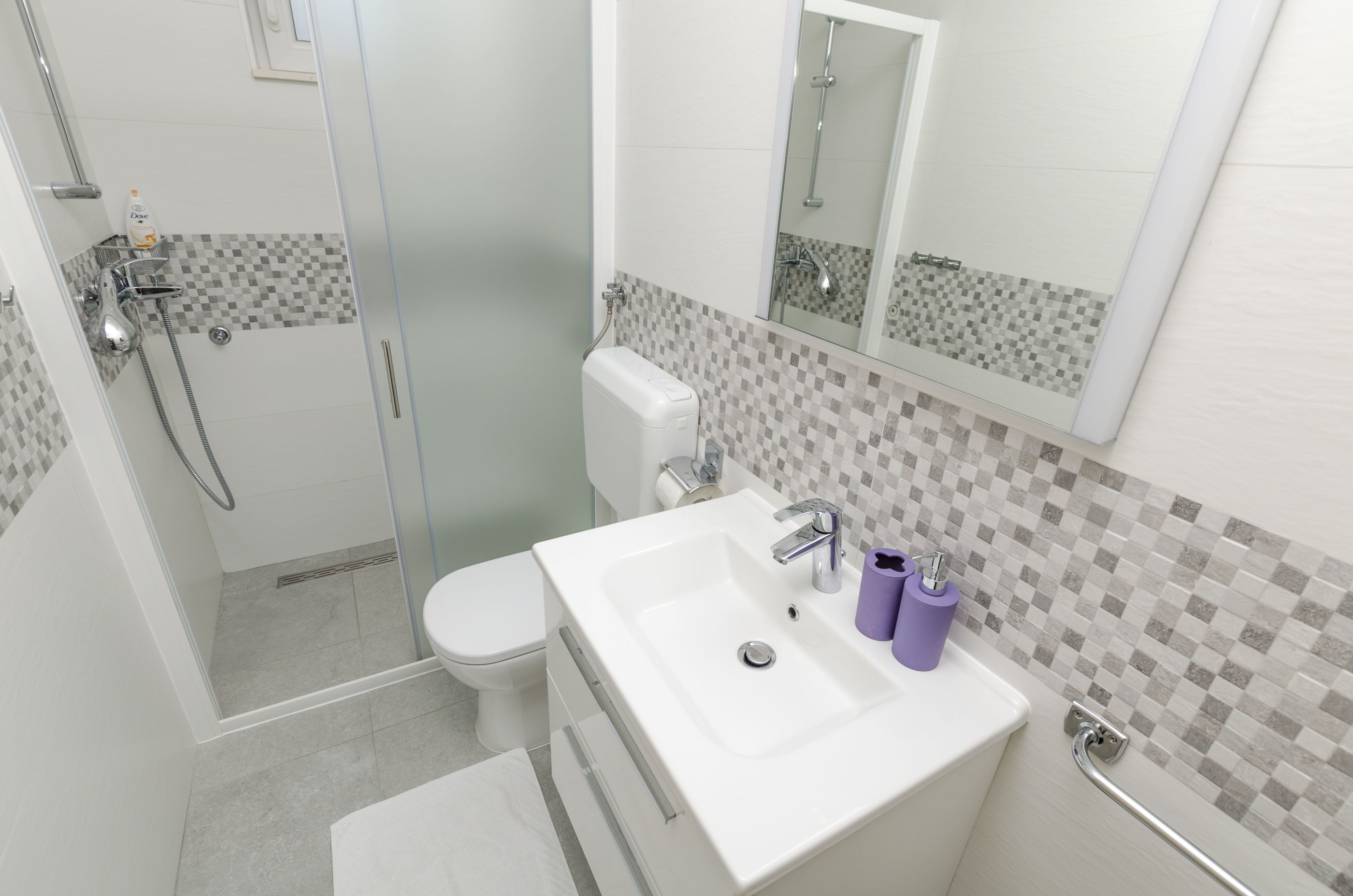 A modern bathroom with a glass-enclosed shower, a white sink with a mirror, and a toilet.