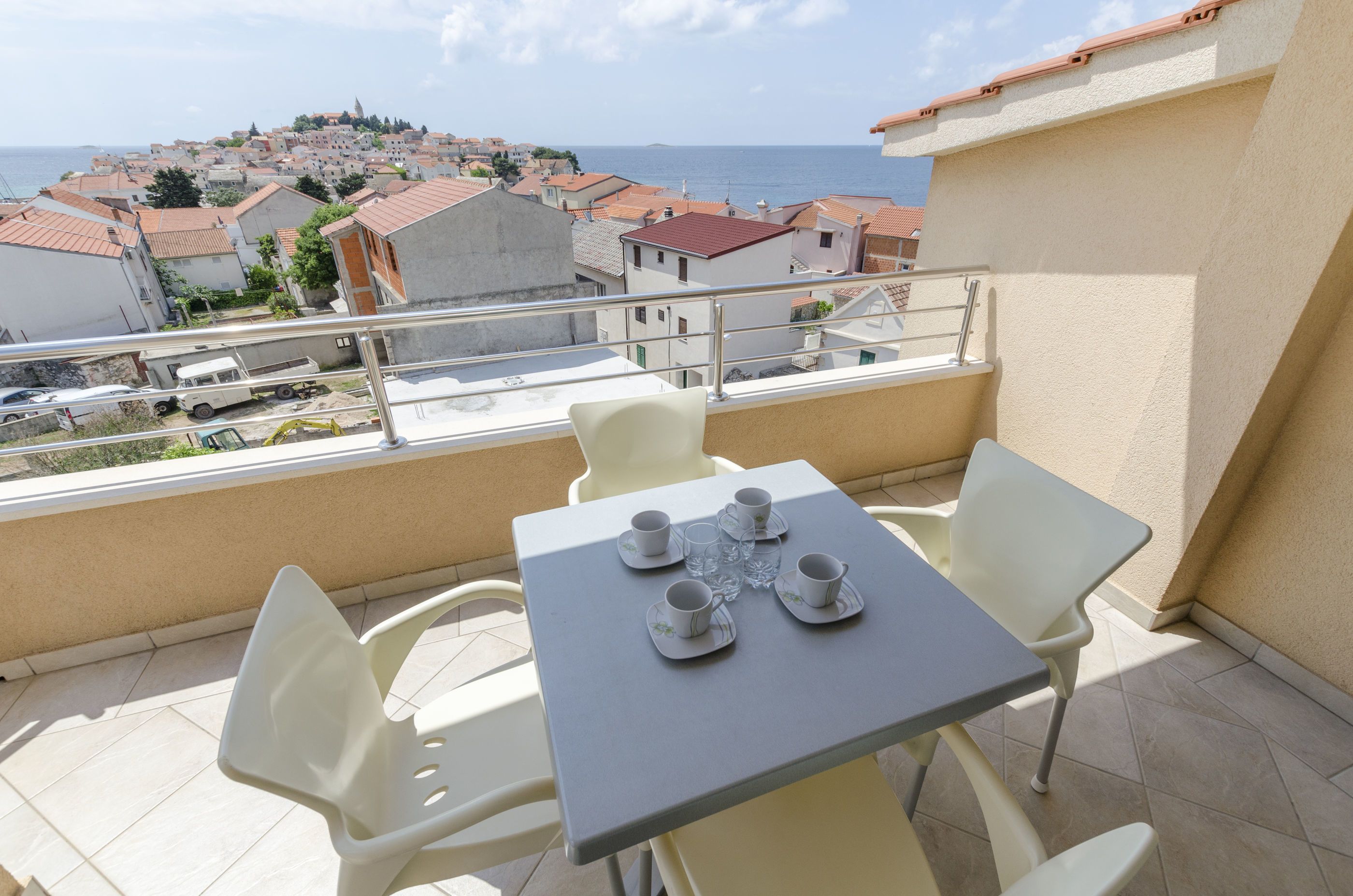 A balcony with a table set for four, overlooking a coastal town.