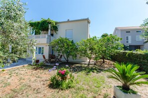 A two-story building with a balcony, a garden with various plants and flowers, and a seating area with chairs. - Apartments Maja (Okrug Gornji)