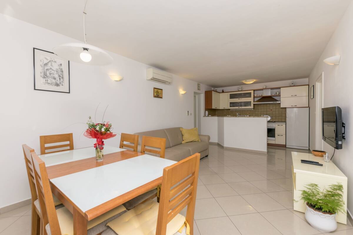 A modern apartment with a dining area, sofa, kitchenette, and a TV.