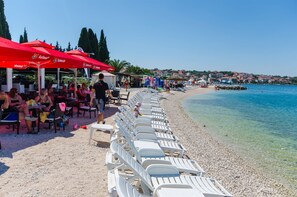 Un restaurante frente a la playa con terraza y sombrillas rojas.