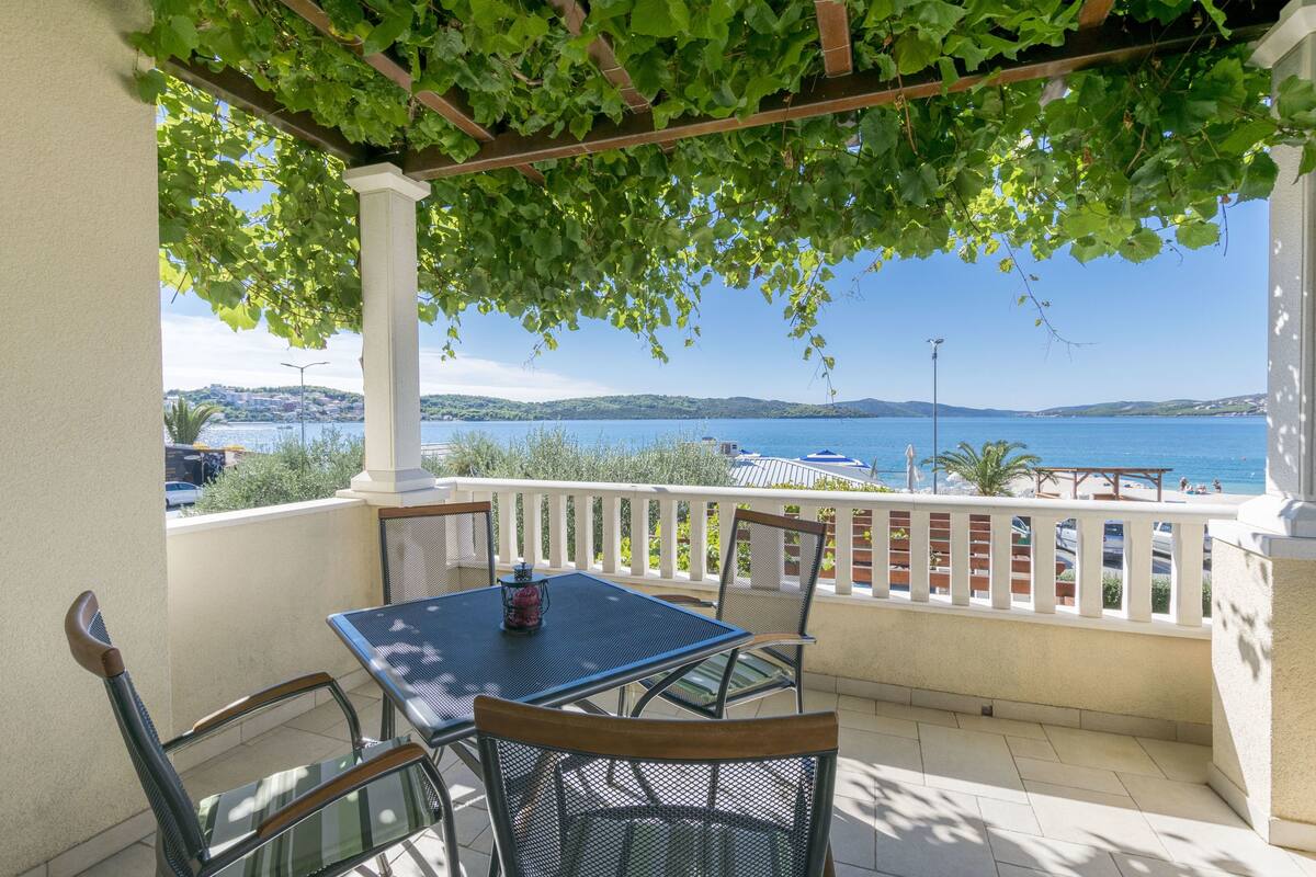 A balcony with a table and chairs, overlooking a body of water and a distant coastline.
